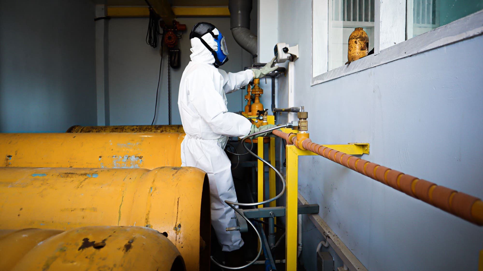 A technician in full protective coverall and respirator working at the valve gear of bulk LPG storage vessels.