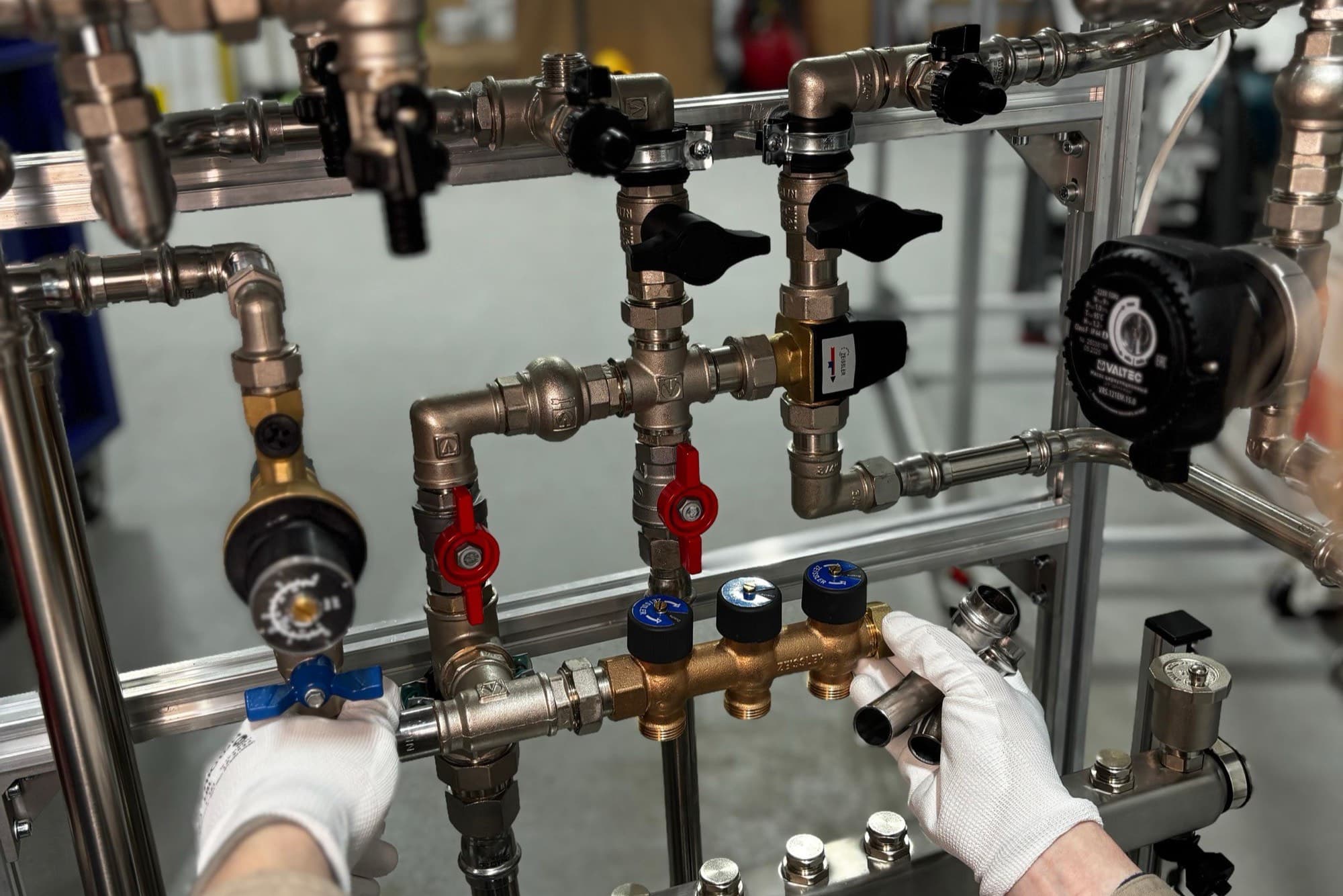 Gloved hands fitting valves and fittings onto a pipework manifold.